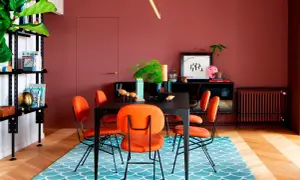 Comedor con paredes color terracota, sillas naranjas vibrantes y una alfombra azul con diseño de escamas. ¡Ideas de colores para pintar un salón audaz!