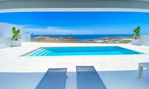 Dos tumbonas invitan a relajarse junto a una moderna piscina blanca, con el mar azul y el paisaje mediterráneo de fondo.