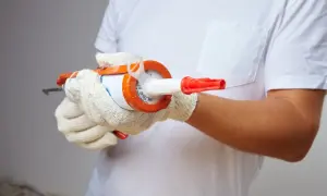 Manos enguantadas sujetan pistola de silicona, preparándose para sellar. ¿Cuánto tarda en secar la silicona?