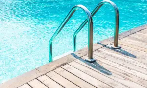 Escalera metálica para entrar a una alberca de agua cristalina, con borde de madera.
