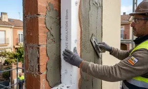 Obrero aplica mortero sobre aislamiento térmico en fachadas. El sistema SATE mejora la eficiencia energética.