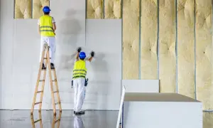 Trabajadores instalan paneles de yeso sobre aislamiento, asegurando la resistencia térmica del edificio.
