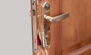 Puerta de contrachapado dañada, lista para reparar. Se ve el mecanismo de la cerradura y la manilla dorada.