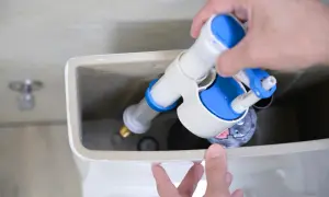 Mano instalando un nuevo mecanismo de descarga para cambiar la cisterna del inodoro.