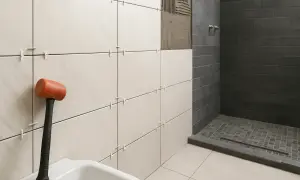 Colocando azulejos con cemento cola. Mazo naranja y azulejos blancos listos para instalar en un baño con ducha oscura.