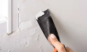 Raspando pintura descascarada de una pared. Un buen truco para pintar paredes es preparar la superficie.