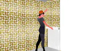 Una mujer con boina naranja y vestido gris está aprendiendo cómo empapelar una pared con un patrón de hojas y olivas.