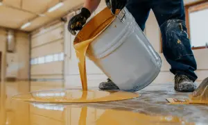 Hombre con guantes vierte pintura amarilla de un cubo para pintar suelo cocina.
