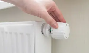 Mano ajustando el termostato para poner calefacción en casa. El radiador blanco está listo para calentar.