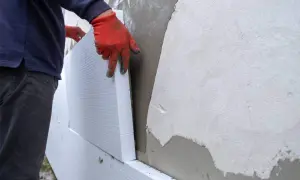 Man con guantes rojos instala paneles de poliestireno para aislamiento exterior fachadas.