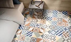 Un suelo con **baldosa hidráulica** de diseño geométrico y colores vibrantes, junto a una cama y una mesita de noche.