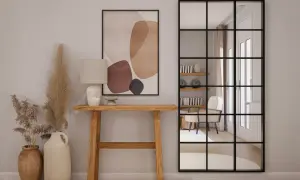 Entradas pequeñas con encanto: consola de madera, lámpara, cuadro abstracto y espejo industrial que refleja un sillón.