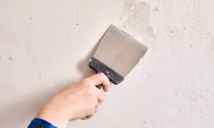 Mano con espátula aplica masilla a una pared irregular.