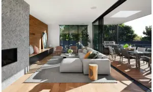 Elegante diseño de salas con chimenea de piedra, sofá modular gris, sillas rosadas y acceso a terraza con comedor exterior.