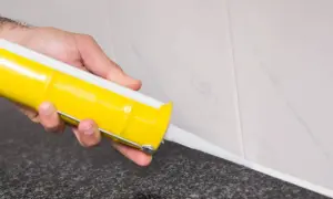 Mano aplicando silicona en juntas con pistola.