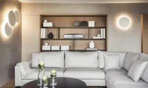 Iluminar un salón moderno con luces de pared circulares y una estantería de madera con objetos decorativos. Sofá gris y mesa negra con jarrones de rosas.