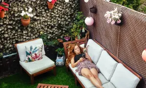 Mujer relajada en un sofá en un patio con césped artificial, luces y plantas. Ideas para decorar patio sin dinero.