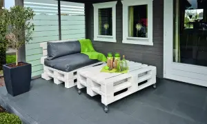 Sofá y mesa de centro hechos con palets pintados de blanco, con cojines grises y manta verde.