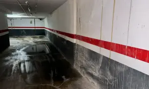 Pasillo de garaje con charcos en el suelo y marcas de humedad por filtración en las paredes pintadas con franjas rojas y grises.