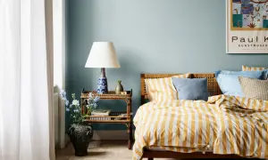 Habitación con paredes azul claro, cama con ropa de cama a rayas amarillas y blancas, y mesita de noche de ratán. Ideas de colores para habitaciones.
