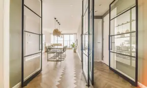 Amplio salón comedor rectangular de 25 metros, con suelo de espiga y separadores de cristal.