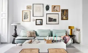 Un sofá azul claro con cojines decorativos y una colección de arte ecléctica en la pared. Ideas de qué poner detrás del sofá: una galería de arte o una estantería.