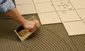 Mano extendiendo cemento cola con llana dentada sobre el suelo para colocar baldosas.