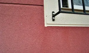 Detalle de juntas de dilatación en fachadas de color rojo y crema, con una ventana enrejada.