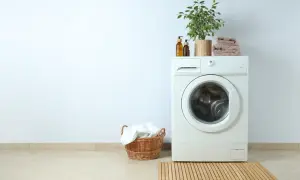 Lavadora blanca con planta y toallas encima. Cerca, una cesta con ropa blanca. La altura lavadora es perfecta para el espacio.