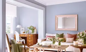 Ideas para decorar casa con poco dinero: sala acogedora con escritorio de madera, sofá blanco, cojines coloridos y flores frescas.