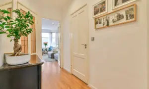 Un pasillo moderno y estrecho con suelo de madera, un bonsái y fotos familiares en la pared.