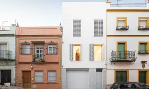 Fachada edificio con ladrillo visto y detalles de azulejos, junto a una moderna construcción blanca y otra amarilla con balcones de forja.