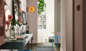 Un recibidor con pasillos con encanto: un escritorio azul, flores rosas, libros y un taburete.