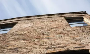 Fachada de ladrillo con sate acabado piedra, mostrando dos ventanas y el cielo azul.