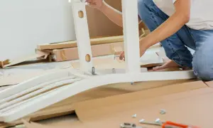 Persona ensambla mueble blanco. Se ve una pletina metálica uniendo piezas. Cajas y herramientas en el suelo.
