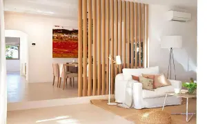 Elegante separador de madera para dividir salón en dos ambientes. Sofá blanco, mesa de centro rústica y cuadro vibrante.