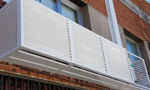 Carcasa blanca con lamas horizontales protege un aire acondicionado en fachada exterior.