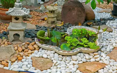 Un sereno jardín zen japonés con un estanque de lotos, linternas de piedra y rocas de diferentes tamaños.