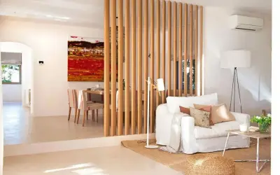 Elegante separador de madera para dividir salón en dos ambientes. Sofá blanco, mesa de centro rústica y cuadro vibrante.
