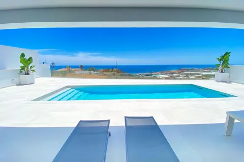 Dos tumbonas invitan a relajarse junto a una moderna piscina blanca, con el mar azul y el paisaje mediterráneo de fondo.