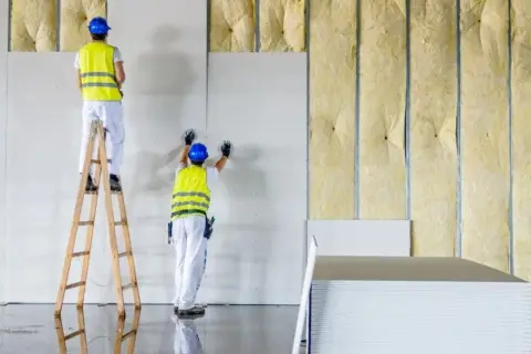 Trabajadores instalan paneles de yeso sobre aislamiento, asegurando la resistencia térmica del edificio.
