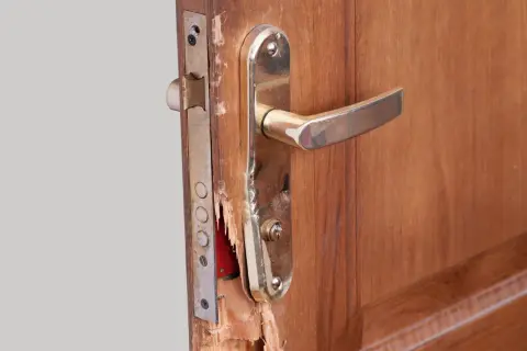 Puerta de contrachapado dañada, lista para reparar. Se ve el mecanismo de la cerradura y la manilla dorada.