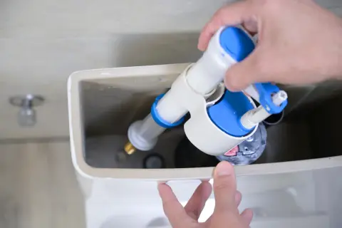 Mano instalando un nuevo mecanismo de descarga para cambiar la cisterna del inodoro.
