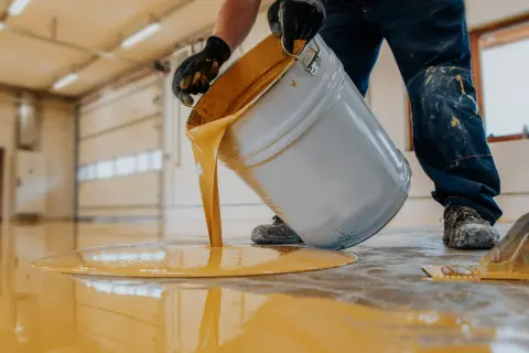 Hombre con guantes vierte pintura amarilla de un cubo para pintar suelo cocina.