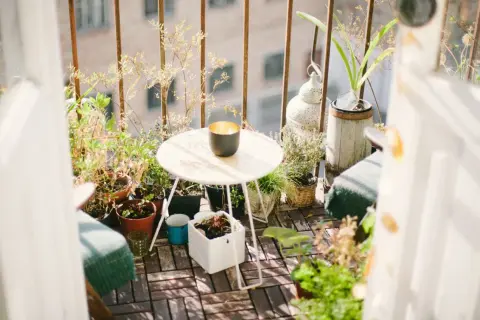 Ideas para aprovechar balcones pequeños: un rincón acogedor con plantas, mesa y silla, creando un oasis verde.