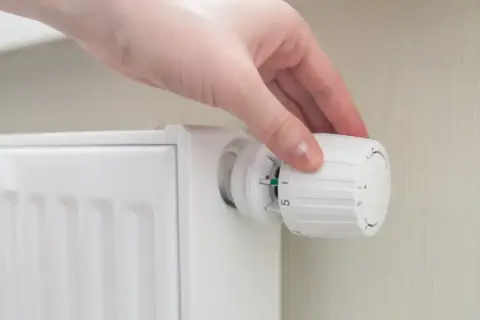 Mano ajustando el termostato para poner calefacción en casa. El radiador blanco está listo para calentar.