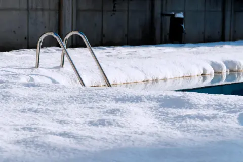 Escaleras de piscina asoman entre la nieve. Un reto para mantener piscina en invierno sin tapar.