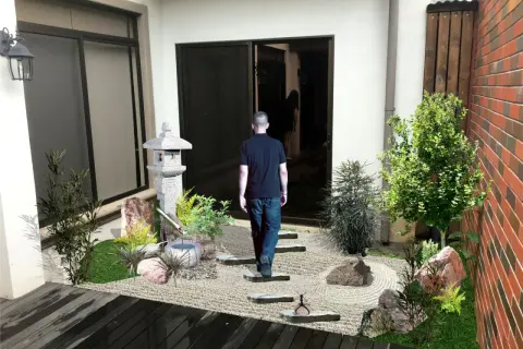 Un hombre camina hacia un sereno **patio jardín japonés en casa**, con una linterna de piedra y un estanque de bambú.