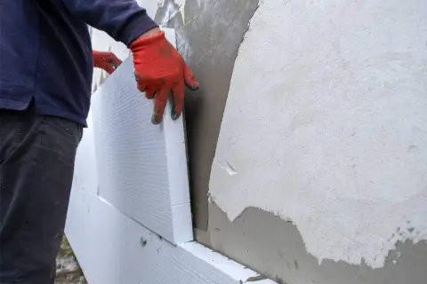 Man con guantes rojos instala paneles de poliestireno para aislamiento exterior fachadas.