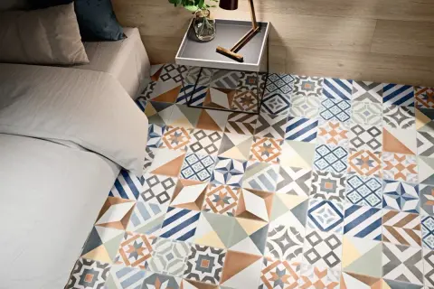 Un suelo con **baldosa hidráulica** de diseño geométrico y colores vibrantes, junto a una cama y una mesita de noche.